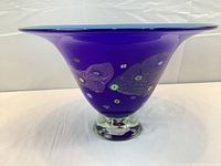 Front view of cobalt blue art glass bowl with floral blossom designs on the side and clear glass base.