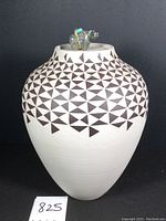 Frontal view of white ceramic pot with black geometric pattern and stone bear finial