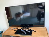 Samsung 46 inch TV on wood table with Blu-ray player and two remotes on top, power cable visible