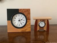 Front view of both Schlabaugh & Sons desk clocks on a wooden surface showing wood grain and clock faces.