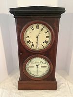 Full front view of oak clock showing upper time dial and lower calendar dial