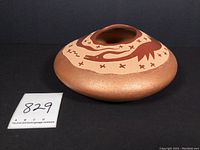 Side view of the small Southwest Pueblo pottery pot showing the rounded flat shape, animal carving pattern, and glittery lower surface.