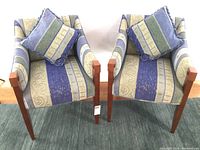 Full view of the two upholstered armchairs with matching throw pillows placed inside each chair, showcasing fabric pattern and wood armrests.
