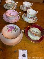 Photo showing all 6 matching teacup and saucer sets, with floral patterns in various colors and gold trims on a wooden table.