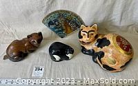 Four assorted cat figurines and decorative piece on fabric background displaying size and details.