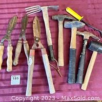 Photo showing assorted hand tools including three pairs of clippers, garden fork, and five hammers with wooden handles
