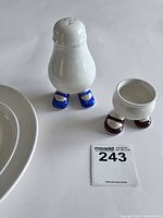 Close-up of salt or pepper shaker with blue shoes, egg cup with maroon shoes, showing condition and design details including crackle glaze
