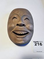Front view of carved wooden smiling face mask on white background.
