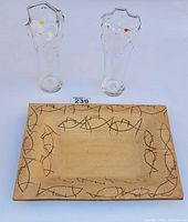 Photo showing two clear art glass vessels with small colored dots on top and the rectangular ceramic plate with fish motif in the background.