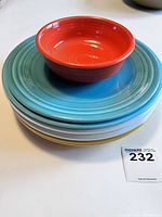Stack of 5 Fiesta plates (turquoise, white, gold) with orange cereal bowl on top.