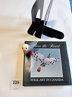 Photo showing black metal bookend, 'From The Heart: Folk Art in Canada' book, and hand-carved seagull figurine.