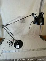 Side view of black Ikea Antifoni desk lamp with adjustable metal arm and round base, cord coiled near base.