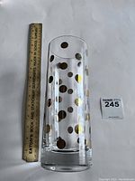Large clear glass cylindrical vase with gold polka dots next to a 12-inch ruler showing height approximately 10 inches