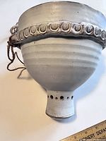 Side view of the ceramic hanging planter showing shape, rope hanger, decorative round motifs and drainage spout with holes at bottom.