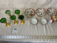 Full set of hand painted green glass liqueur glasses and Asian tea set on cloth background with ruler.