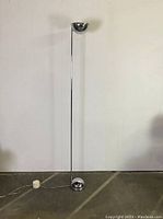 Full front view of the tall chrome torchiere lamp against a plain white wall.