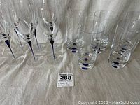 Set showing 6 white wine glasses with slender stems featuring blue detail, and 5 cylindrical high ball glasses with blue dots at base.