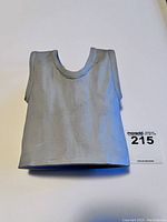 Front view of grey ceramic vase shaped like sleeveless shirt next to lot number card