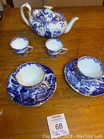 Photo showing the complete set including teapot, two teacups with saucers, and two smaller child's cups on a wooden surface.