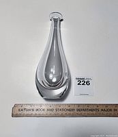 Front view of tall teardrop-shaped clear glass bud vase with ruler for scale showing approximately 9.75 inches height.