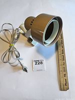 Vintage plastic clamp lamp lying next to a ruler for size reference, showing brown shade and white clamp base with attached power cord.