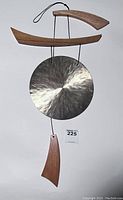Full view of the Woodstock Chimes Emperor Gong wind chime showing metal gong, wooden top hanger, and bottom sail.