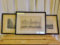 Three framed antique European prints with black frames and cream mattes, showing architectural and street scenes.