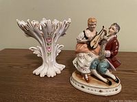 Photo showing porcelain couple figurine and hand-painted vase on a brown wooden surface