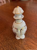 Front angle view of the antique Irice hand-painted porcelain perfume bottle with stopper on a wooden surface.