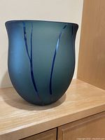 Single photo showing a large hand-blown glass bowl with matte teal finish and blue reflective strips resembling tree branch design.