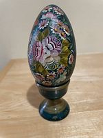 Image of Russian hand painted decorative egg from 1990, showing floral painted decoration and pedestal base in green and gold tones