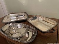 Four silver Reed & Barton serving dishes with decorative beading including a bowl with serving spoon and three rectangular trays with handles, some tarnishing present.