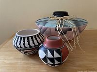 Photo of three hand-crafted Southwestern pottery bowls: two small bowls with geometric patterns and one larger wedding bowl with tied straw decoration.