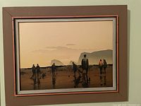 Wood-framed silkscreen print showing clam diggers on beach at sunset with coastal rock formations in background