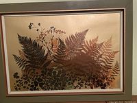 Silk screen print showing layered fern silhouettes in brown, gold and green tones on beige, framed in wood