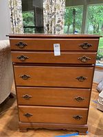 Front view of wooden chest with four drawers and brass handles in a living room setting.