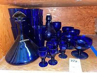 Photo showing entire glassware set on wood shelf, including decanter, goblets, dessert cups and drinking glasses.