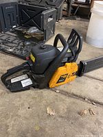 Poulan Pro 50cc chainsaw with black body, yellow side panel, metal chain bar, and plastic grips lying on concrete floor near open black carrying case.