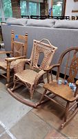 Three children's rocking chairs grouped together. Two wooden rocking chairs with carved backs and one wicker rocking chair which has a damaged rocker base.