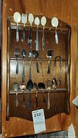 Front view of wooden rack displaying 18 collector spoons and some forks with different handle designs.