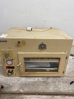 Front view of cream-colored Grumbach egg incubator showing rectangular housing, power cord, front door with window