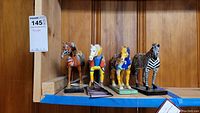 Five horse and zebra figurines displayed on shelf, showing varied artistic paint styles and bases