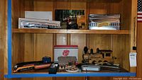 Wide view of shelf showing multiple train models including a wooden engine, train house, and boxed game on top shelf.