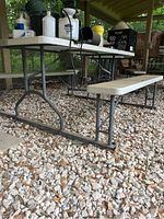 Side view of the picnic table showcasing metal legs and plastic bench seat on rocky ground outdoors.