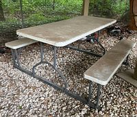 Photo showing side angle of weathered outdoor picnic table and benches on gravel and leaves under shelter.