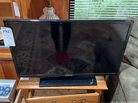 Front-on photo of the Samsung 26 inch TV on a wooden stand, screen blank and powered off.