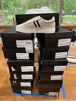 Stack of black shoeboxes labeled 'Ccocci' with varying shoe sizes 7-10. One beige shoe displayed on top.