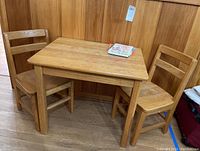 Overall view of wooden children's table with two chairs positioned around it, books on table