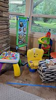 Overview of children's activity table, yellow toddler chair, spiral race track toy, ottoman, basket, and books.