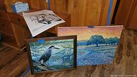 Framed bird-themed painting on wood and canvas landscape painting with trees and field, showing both paintings side by side.